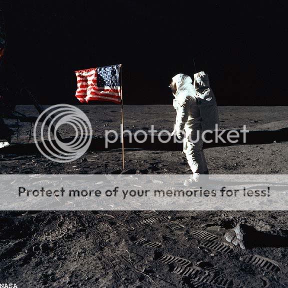Astronaut Edwin E. Buzz Aldrin, Jr., lunar module pilot of the first lunar landing mission, is beside the U.S. flag during an Apollo 11 moon walk. The Lunar Module (LM) is on the left, and the footprints of the astronauts are clearly visible in the soil of the moon.  Image ©NASA.  All rights reserved. 