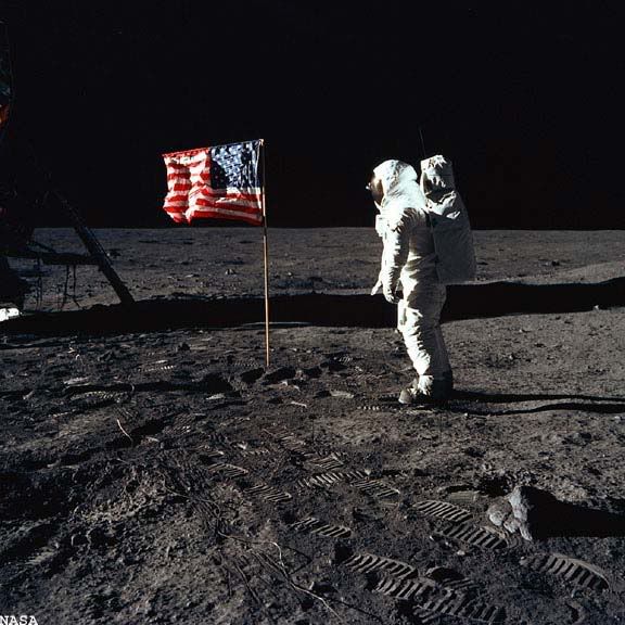 Astronaut Edwin E. Buzz Aldrin, Jr., lunar module pilot of the first lunar landing mission, is beside the U.S. flag during an Apollo 11 moon walk. The Lunar Module (LM) is on the left, and the footprints of the astronauts are clearly visible in the soil of the moon.  Image ©NASA.  All rights reserved. 